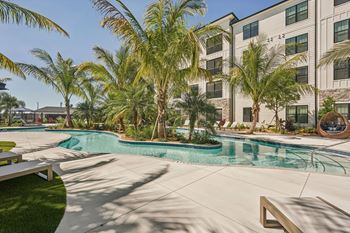 A pool surrounded by palm trees and a building in the background
